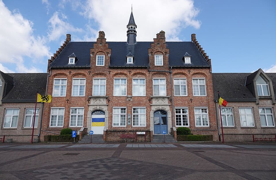 Gemeentehuis met Belgische en Oekraïense vlaggen voor een heldere blauwe lucht.