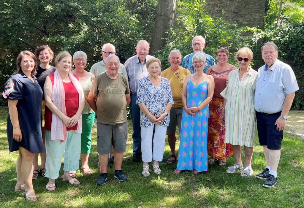 Groep ouderen en vrijwilligers in park tijdens bijeenkomst.