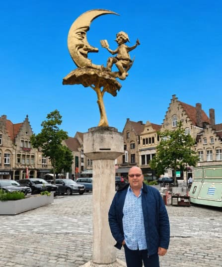 Beeld van een man die op een maan zit met een boek in de hand.