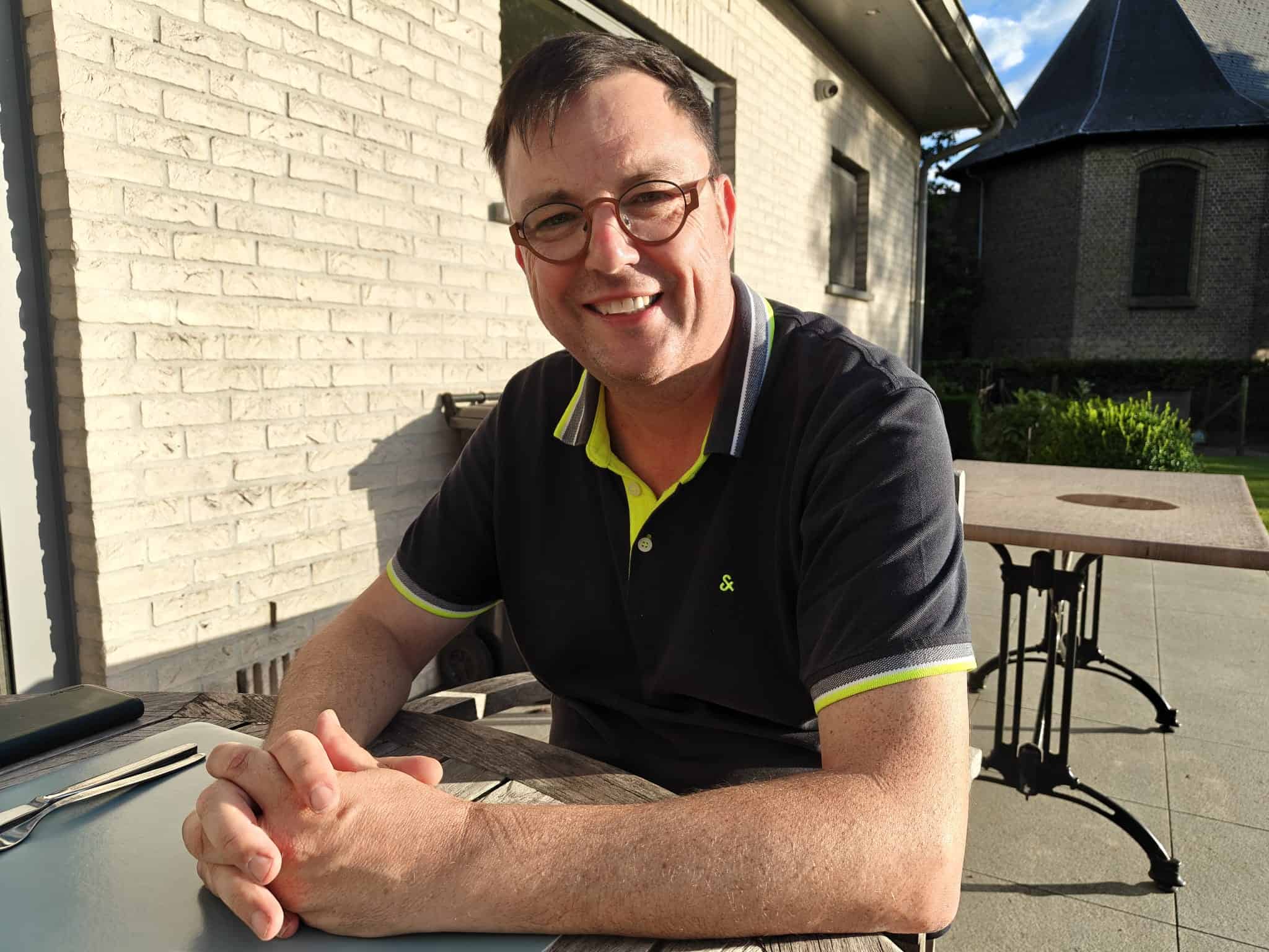 Man met bril en glimlach zit buiten aan tafel.